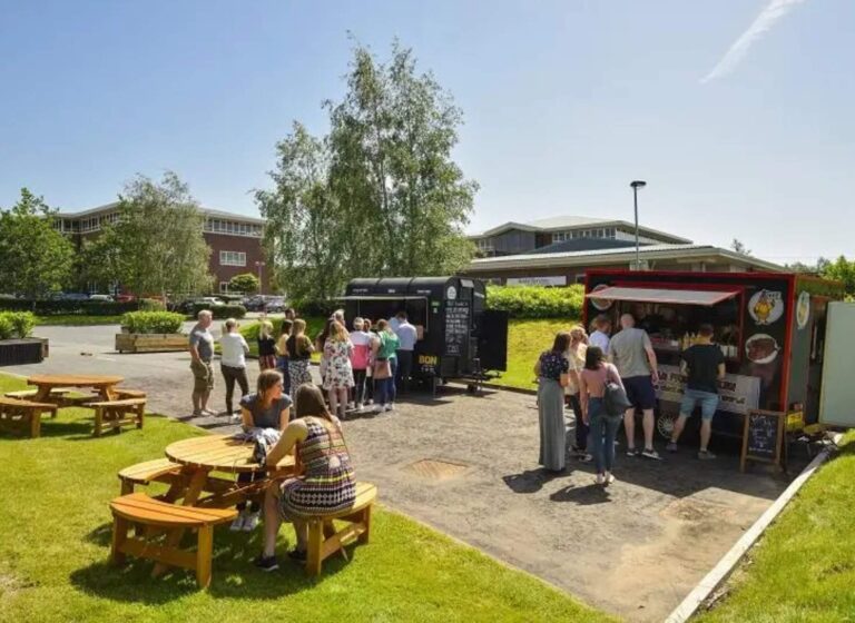 two food trucks and benches with people queueing