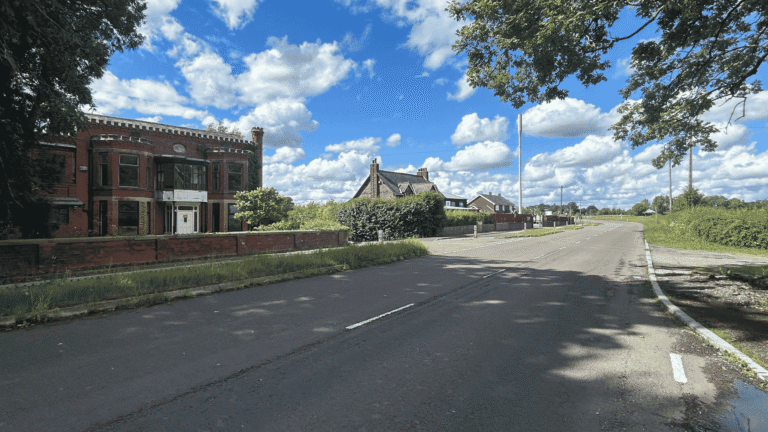 View of large red brick house on the left with 2-lane road in countryside