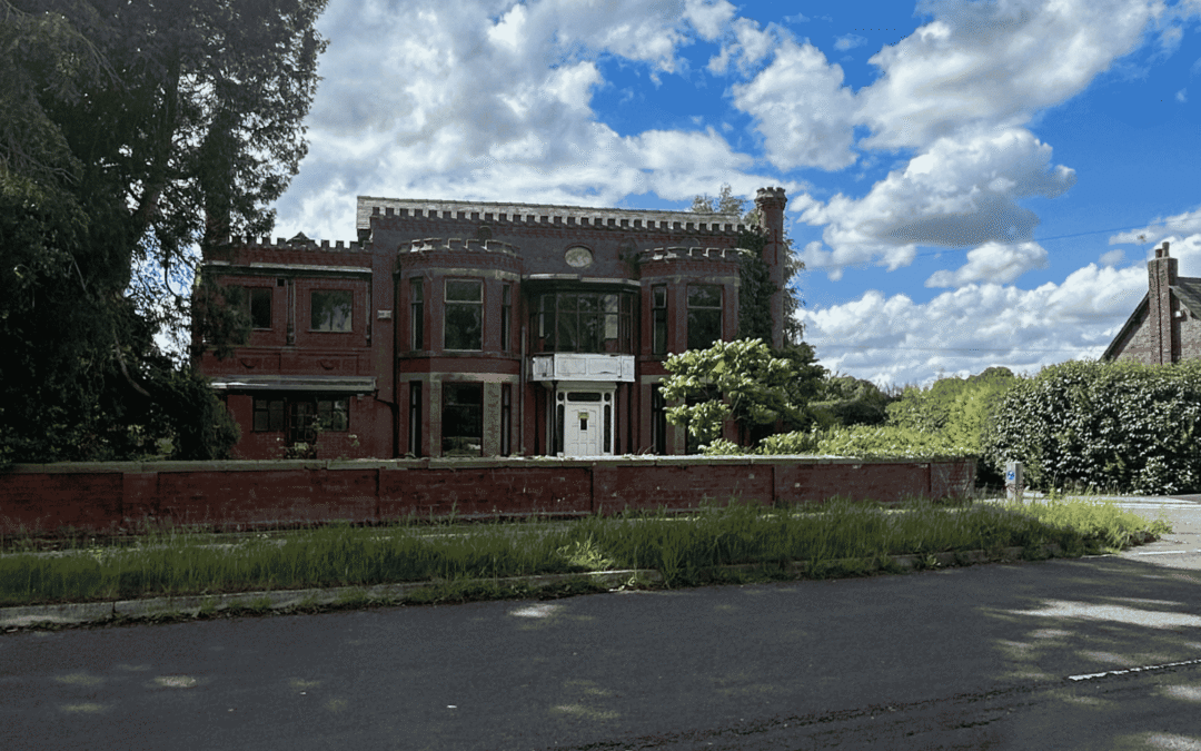 road in foreground with large red brick house with turrets in background